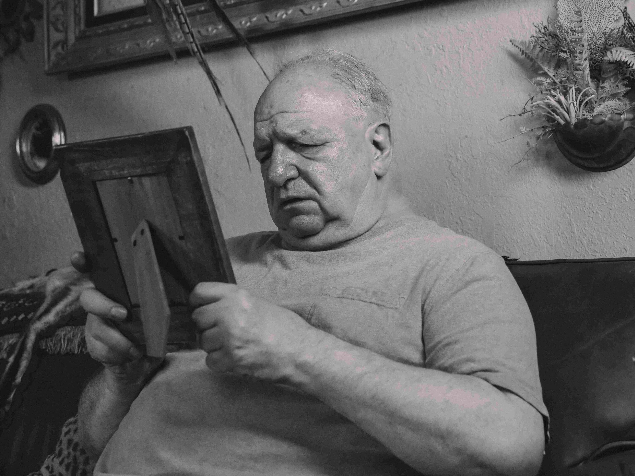 Photo by Kindel Media: https://www.pexels.com/photo/a-grayscale-photo-of-an-elderly-man-holding-a-wooden-frame-8172284/